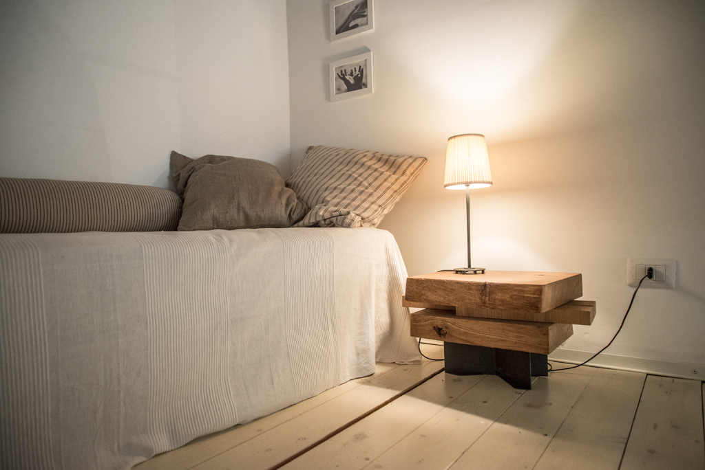 Via delle Orfane by CON3STUDIO - Desk Lamp On Wooden Table Beside Grey Bed Added Near Framed Pictures On Wall Via delle Orfane by CON3STUDIO - Desk Lamp On Wooden Table Beside Grey Bed Added Near Framed Pictures On Wall