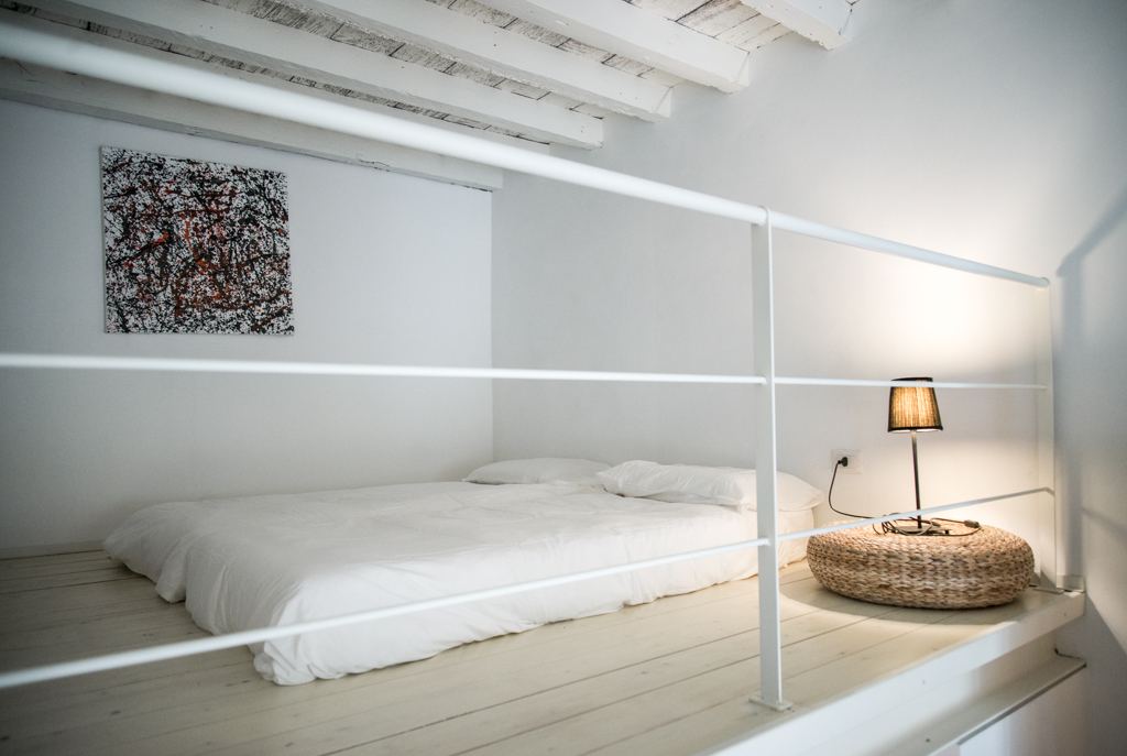 Via delle Orfane by CON3STUDIO - White Bed Land On Floor Added Near Desk Lamp On Round Shaped Table Via delle Orfane by CON3STUDIO - White Bed Land On Floor Added Near Desk Lamp On Round Shaped Table